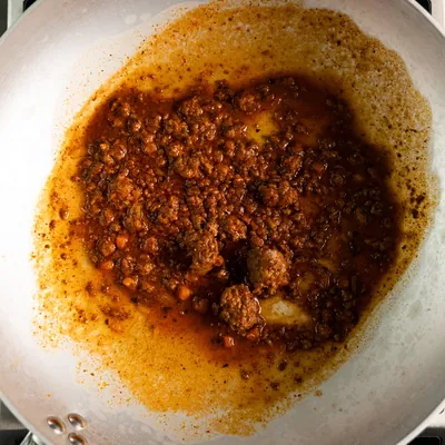 Il ragù che si allarga a macchia sul fondo chiaro della padella